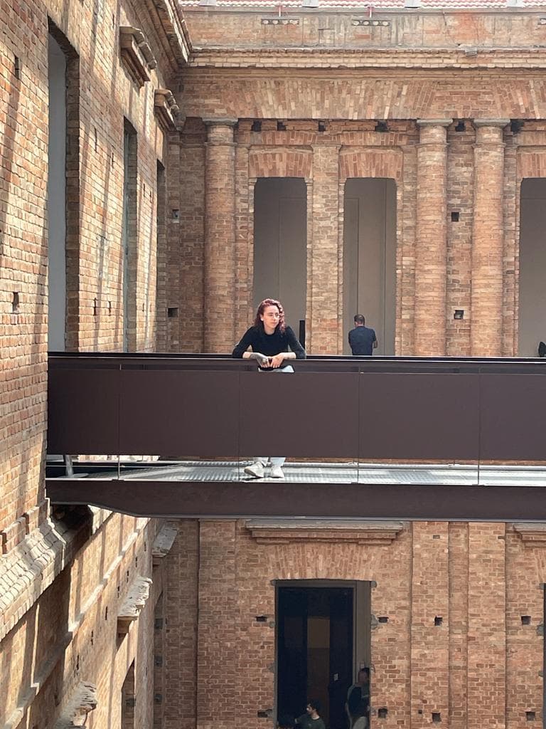Vanessa em uma passarela entre paredes de tijolos na Pinacoteca de São Paulo
